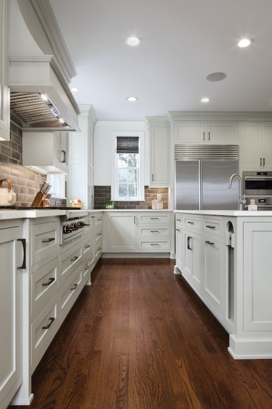 A kitchen with off-white cabinets, medium toned wood flooring, and ample walkway space to move from countertops to the kitchen island. 
