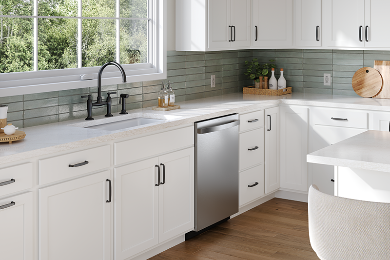 This image pans across bright-white kitchen cabinets with dark metal hardware, as lower cabinets and upper cabinets are in view. The entire kitchen features white as the focus color, and a soft ocean green as the tile-accented backsplash. 