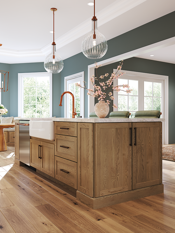 A medium-toned natural wood kitchen island with cabinets, built-in sink, a light-colored granite countertop, and pretty vase of cherry blossoms set on top. The space is surrounded by natural lighting. 