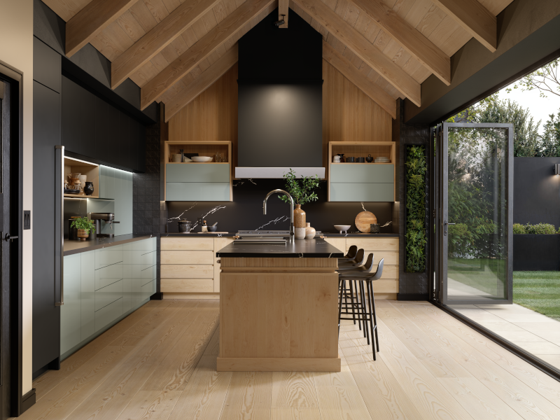 Multiple kitchen cabinet finishes create a cohesive, layered design in this photo, with light-wood toned lower cabinets and washed-out blue-toned cabinets. The kitchen is accented by dark grey paint, a vaulted A-frame ceiling, and fully open glass doors to the right that lead to the backyard. 