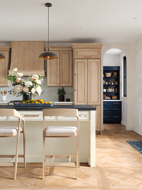 This kitchen snapshot shows part of a kitchen-island with high stools, a large bouquet of garden flowers, and the butler's pantry in the distance, with accents of light-wooden cabinetry and deep blue. 