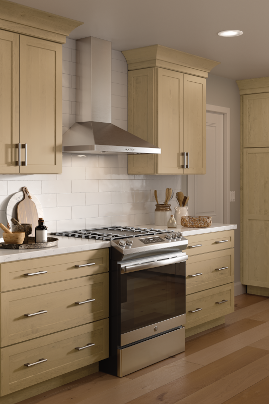 A kitchen stove with matching silver range hood, and soft, sand-colored kitchen cabinets with earth-toned color palette. 