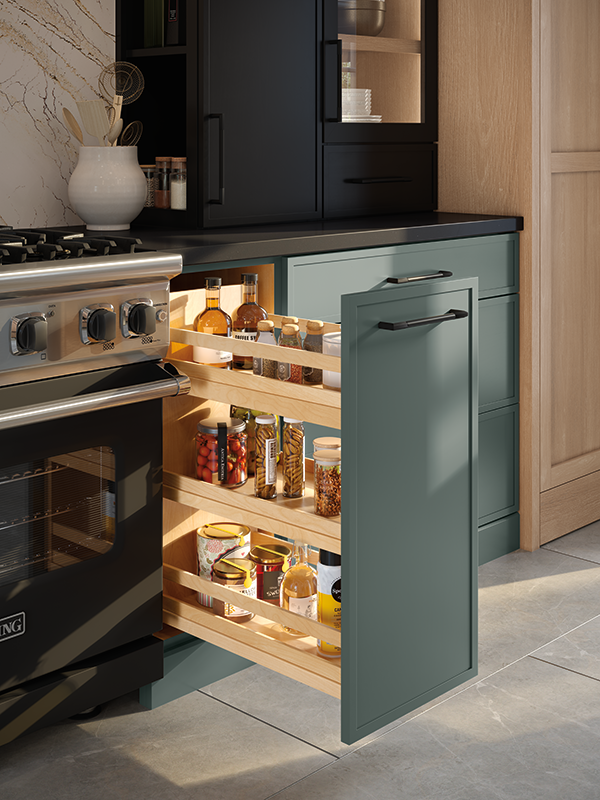 A side pantry pull-out of a kitchen cabinet reveals three organized internal shelves containing cooking ingredients and spices. The exterior of the pull-out drawer features a dark sage green exterior, blending into the surrounding cabinetry when pushed back into place. 