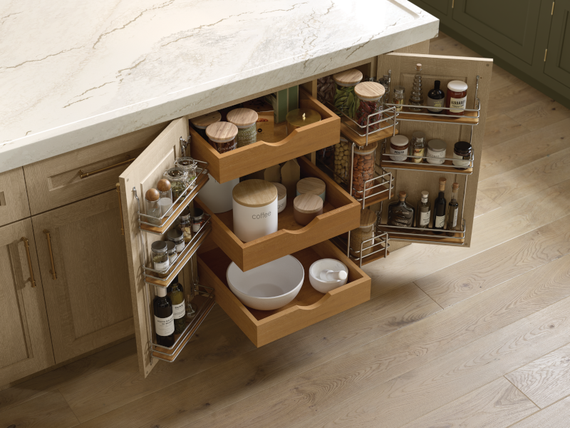 Light-toned lower kitchen cabinet doors are opened, revealing many custom organizational details inside. This includes three pull-out drawers in the center, small racks on the interior of both doors to hold spices, and a small pull-out section for other dry goods, all arranged in clear jars and modern canisters. 