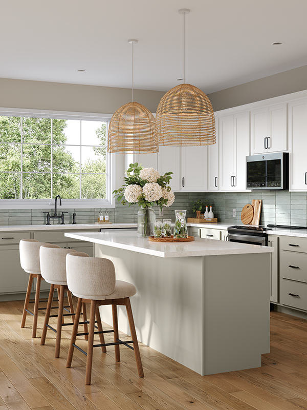 This kitchen looks aesthetically curated, featuring tones of off-white, light green, and washed out blues for an airy feel. Two wicker lampshades hang over the kitchen island, while a bouquet of flowers rests on the white marble island countertop. Three barstools with natural-toned seats are set at the island bar. 