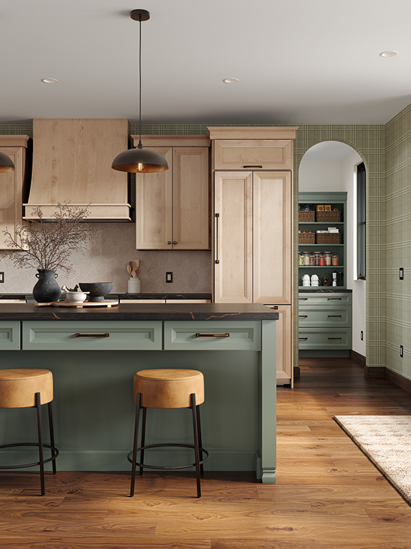 This shows a snapshot of a kitchen, looking from the teal-colored kitchen island to the counter in the distance, with light-toned natural wood cabinets above. In the distance, we see the arched entryway to the butler's pantry on the right. Leather, backless barstools are set at the kitchen island. 