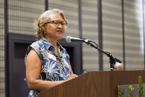 Women in blue with glasses speaking at a podium.