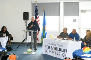 A group of people sitting at tables at an event while a man speaks to them.