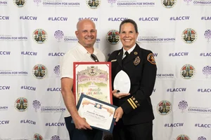 2 people smiling and holding up a few awards.