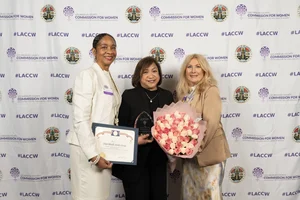 3 women smiling and holding up awards and flowers.