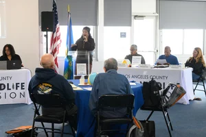 A group of people sitting at tables at an event while a woman speaks to them.