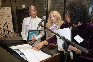 3 women discussing paperwork at a podium.