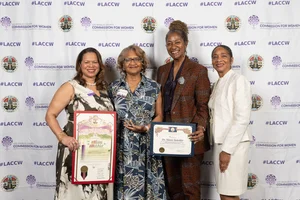 Supervisor Mitchell smiling for a photo with 3 other women while holding up a couple of awards.