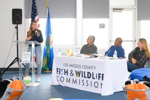 A group of people sitting at tables at an event while a woman speaks to them.