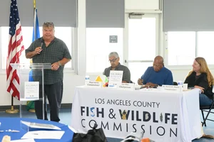 A group of people sitting at tables at an event while a man speaks to them.