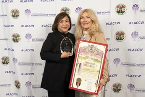 2 women smiling for a picture while they each hold up an award.