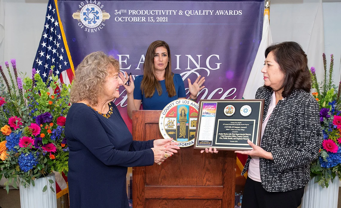 Supervisor Solis at the Productivity & Quality Awards with two other women at the podium.