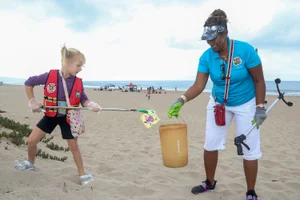 Supervisor Mitchell cleaning up litter at the beach, helping a young girl