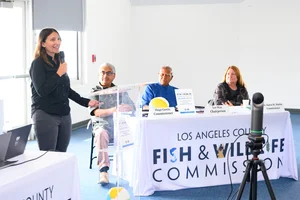 A group of people sitting at tables at an event while a woman speaks to them.