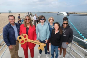 Supervisor Mitchell holding a large key in a group photo in front of water