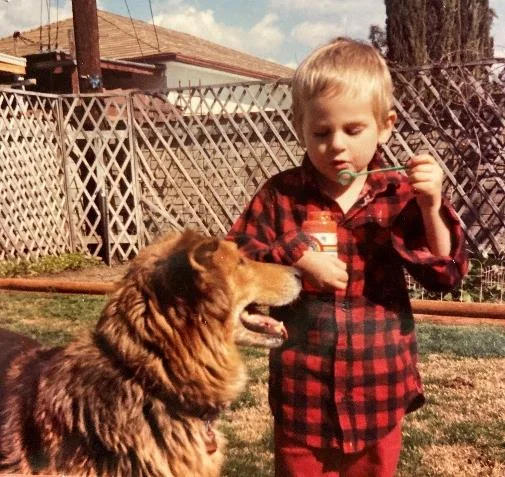 young child holding a container of bubbles standing next to a dog.
