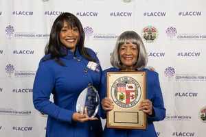 2 women smiling and holding up awards.