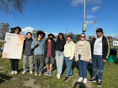 A group of kids/young adults posing for a picture while holding up a sign with words too small to read.