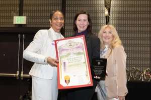 3 women smiling while holding up a couple awards.