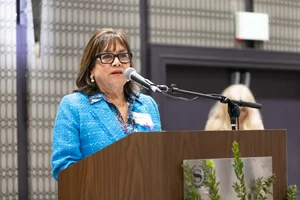 Woman in blue wearing glasses speaking at a podium.