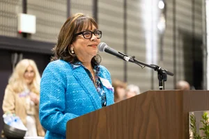 Woman in blue wearing glasses speaking at a podium.