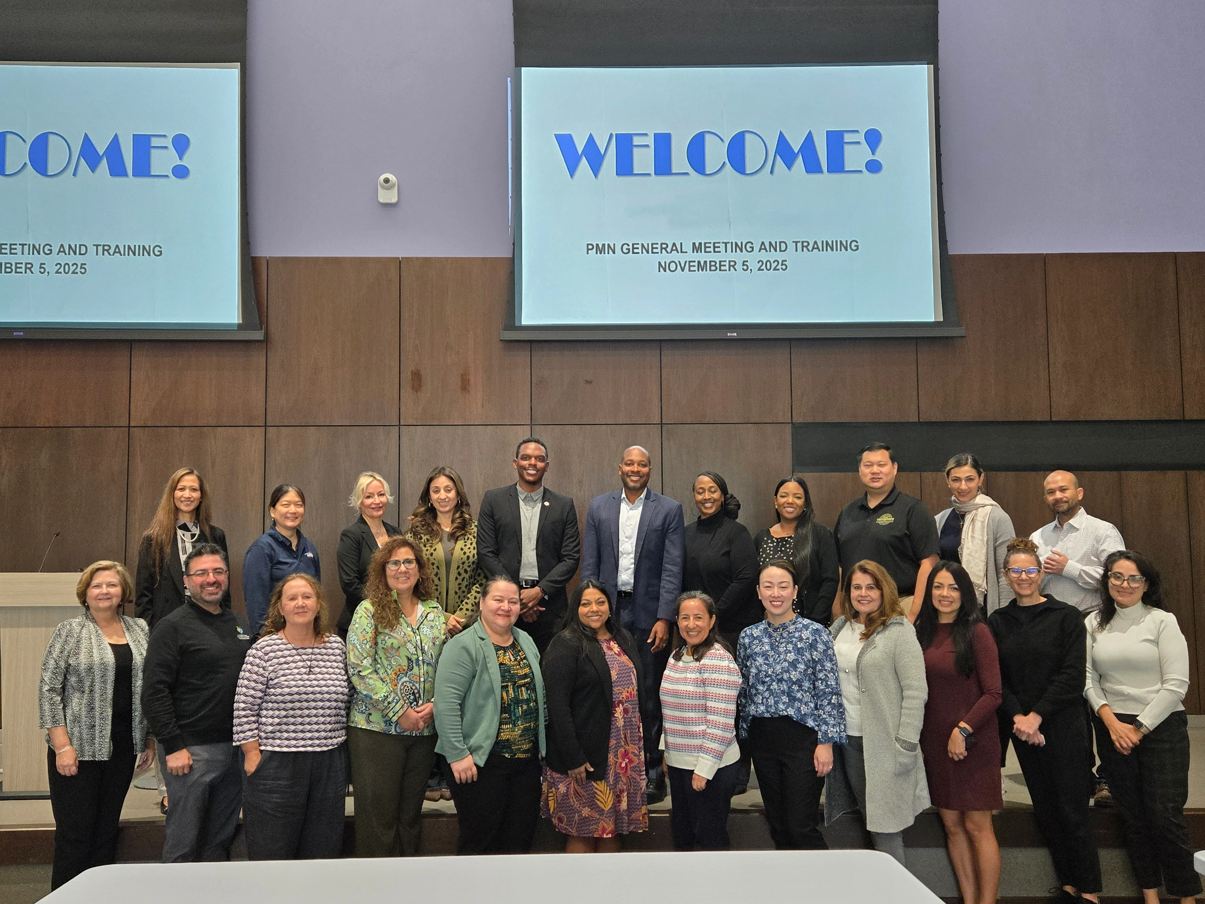 group photo with a large welcome screen above the group of people