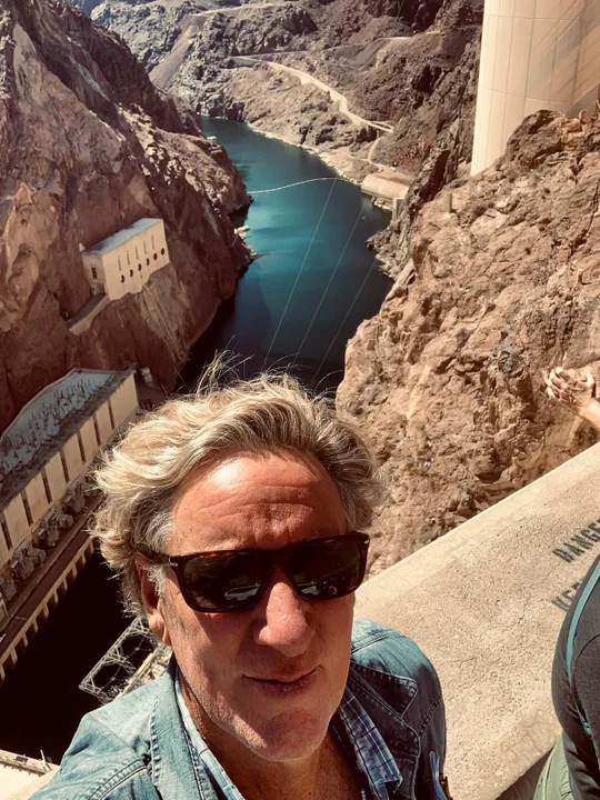 Man in sunglasses taking a selfie in front of an aqueduct.