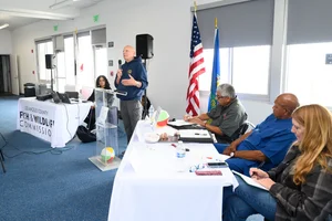 A group of people sitting at tables at an event while a man speaks to them.