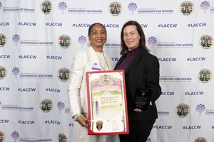2 women smiling for a photo while holding up an award.