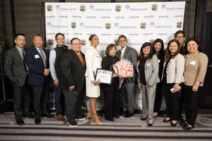 group of people smiling while holding up an award and flowers.