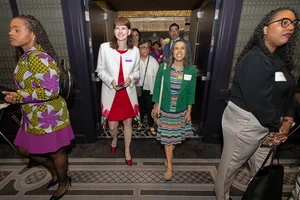 2 women smiling and walking through a doorway.