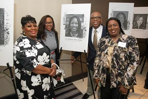 A group of 4 people posing for a photo in front of another woman's photo.