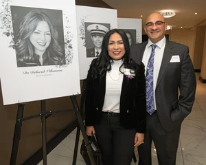 Man and woman posing for a photo in front of a memorial picture of another woman.