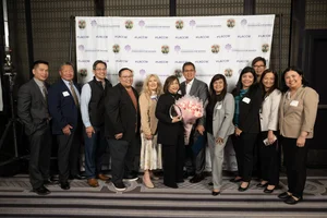 group of people smiling while holding up an award and flowers.