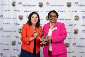 Supervisor Holis and another woman smiling and holding an award together.