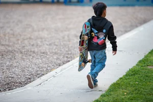 A kid walking down the sidewalk holding a skateboard