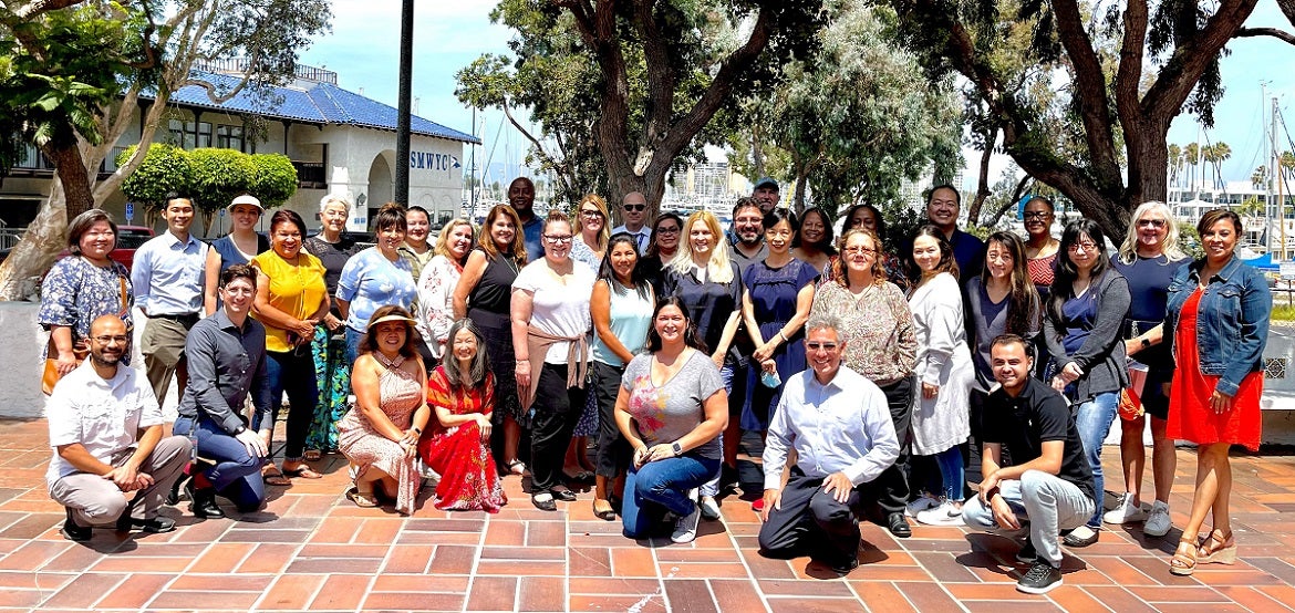 Group photo of adults in front of a building and trees.