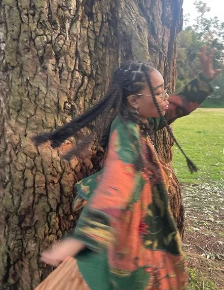 Young woman posing in front of a tree.