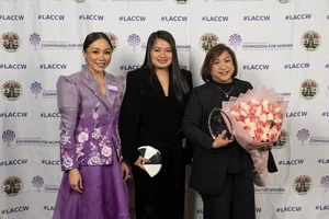 3 women smiling while holding up a couple awards and flowers.