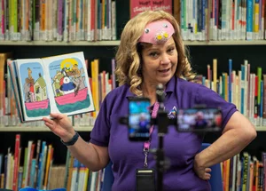 woman posing for a photo with a kids book in her hand in front of a shelf of books.