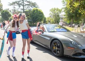 Supervisor Barger waving from a car with two girls dressed in red, white and blue posing outside.