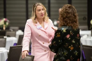 2 women speaking to each other surrounded by tables and chairs.