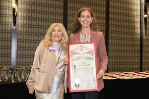 2 women smiling and holding up an award.