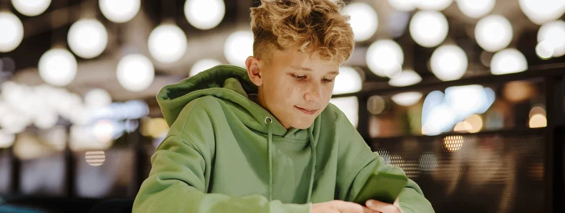 Smiling boy using smart phone in illuminated food court. Surprising New Study About Teens and Texting. 