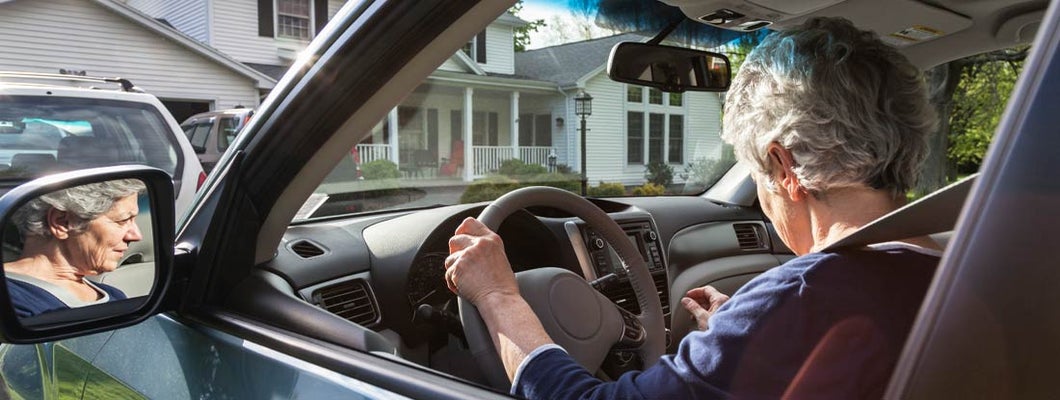 Woman in car pulling out of driveway from home. Find Maine Umbrella Insurance.